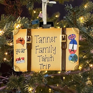 May include: A brown suitcase-shaped Christmas ornament with the text "Tanner Family Tahiti Trip" and various travel stickers.