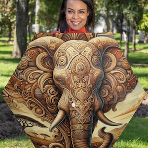 Puede incluir: Un paraguas hexagonal con una ilustración detallada de la cabeza de un elefante en tonos dorados y marrones. La cabeza del elefante está adornada con intrincados patrones y diseños, creando una apariencia decorativa y artística.