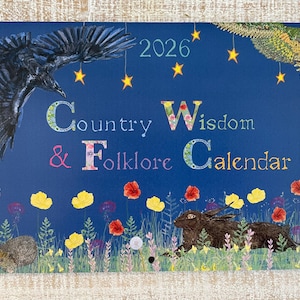 Puede incluir: Calendario 2026 con fondo azul oscuro que presenta ilustraciones de un cuervo, un búho, un erizo y liebres. El texto "Country Wisdom & Folklore Calendar" se muestra con detalles florales y flores amarillas y rojas.