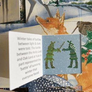 Pu&ograve; includere: Pagina aperta di un calendario dell'Avvento a tema invernale. La pagina presenta un'illustrazione di una volpe e di un uccello. Una piccola carta mostra due figure con spade. Il testo sulla carta recita: "Winter tales of battles between light & dark were told."