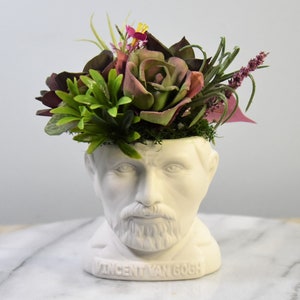 May include: White ceramic planter shaped like a bust of Vincent van Gogh, with a crown of faux succulents and flowers in shades of pink, green, and purple.