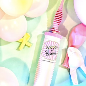 May include: A pink and white balloon pump with a pink nozzle, surrounded by pastel balloons. The pump has the text "Love & Whimsy" on the side. Yellow and pink deflated balloons are also visible.