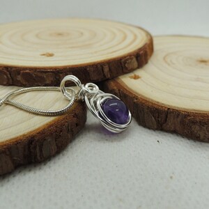 May include: A silver wire wrapped pendant featuring a round, purple amethyst gemstone. The pendant is hanging from a silver chain.