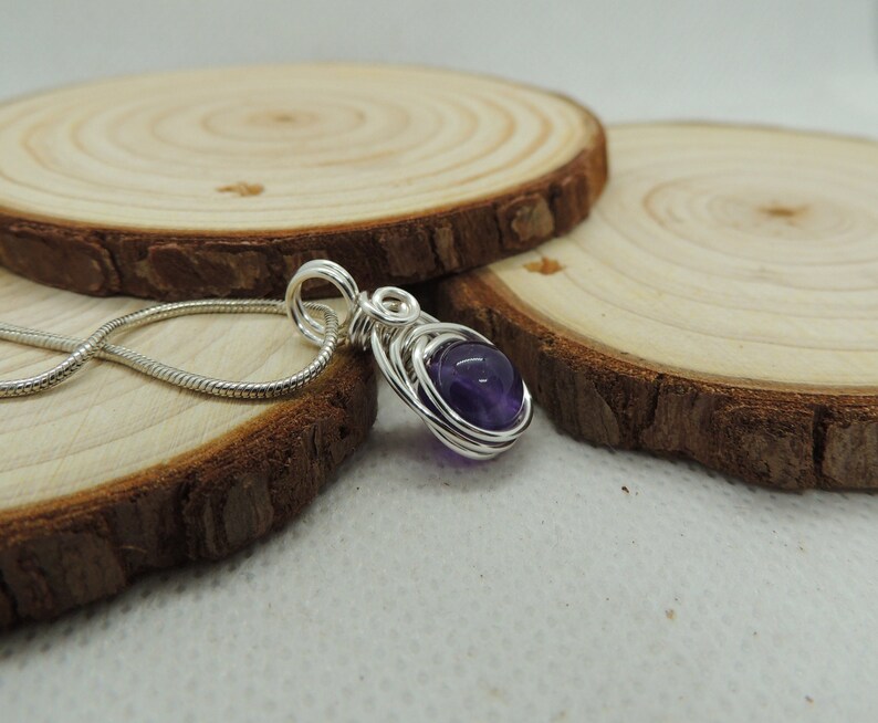 May include: A silver wire wrapped pendant featuring a round, purple amethyst gemstone. The pendant is hanging from a silver chain.