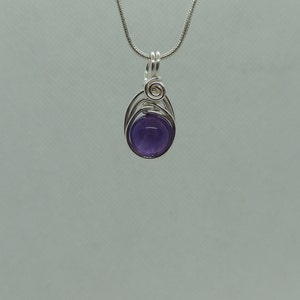 May include: A silver chain necklace with a purple amethyst gemstone pendant. The pendant is wrapped in silver wire and has a simple design.