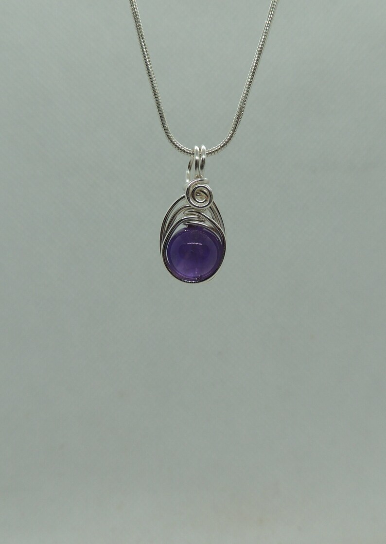 May include: A silver chain necklace with a purple amethyst gemstone pendant. The pendant is wrapped in silver wire and has a simple design.