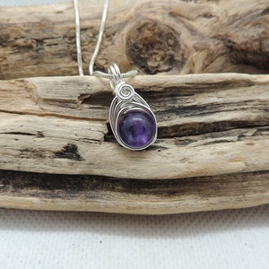 May include: A silver wire wrapped pendant featuring a round, purple amethyst gemstone.