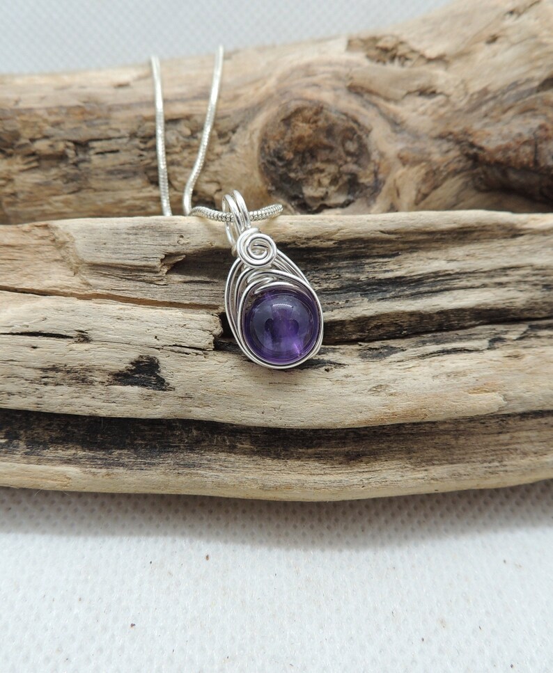 May include: A silver wire wrapped pendant featuring a round, purple amethyst gemstone.