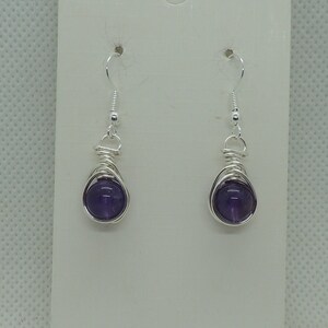 May include: A pair of silver wire wrapped earrings with amethyst stones.