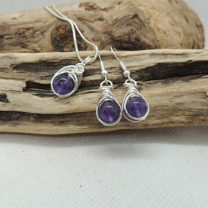 May include: A set of amethyst gemstone jewelry featuring a pendant necklace and matching earrings. The amethyst stones are wrapped in silver wire and have a deep purple hue.