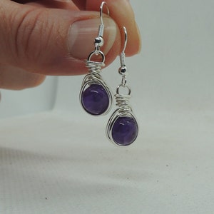 May include: A pair of silver wire wrapped earrings with amethyst stones. The earrings are dangling and have a simple design.