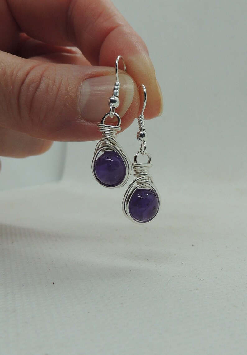May include: A pair of silver wire wrapped earrings with amethyst stones. The earrings are dangling and have a simple design.
