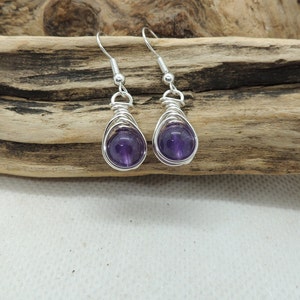 May include: A pair of silver wire wrapped earrings with amethyst gemstones. The earrings are dangle style and have a simple design.