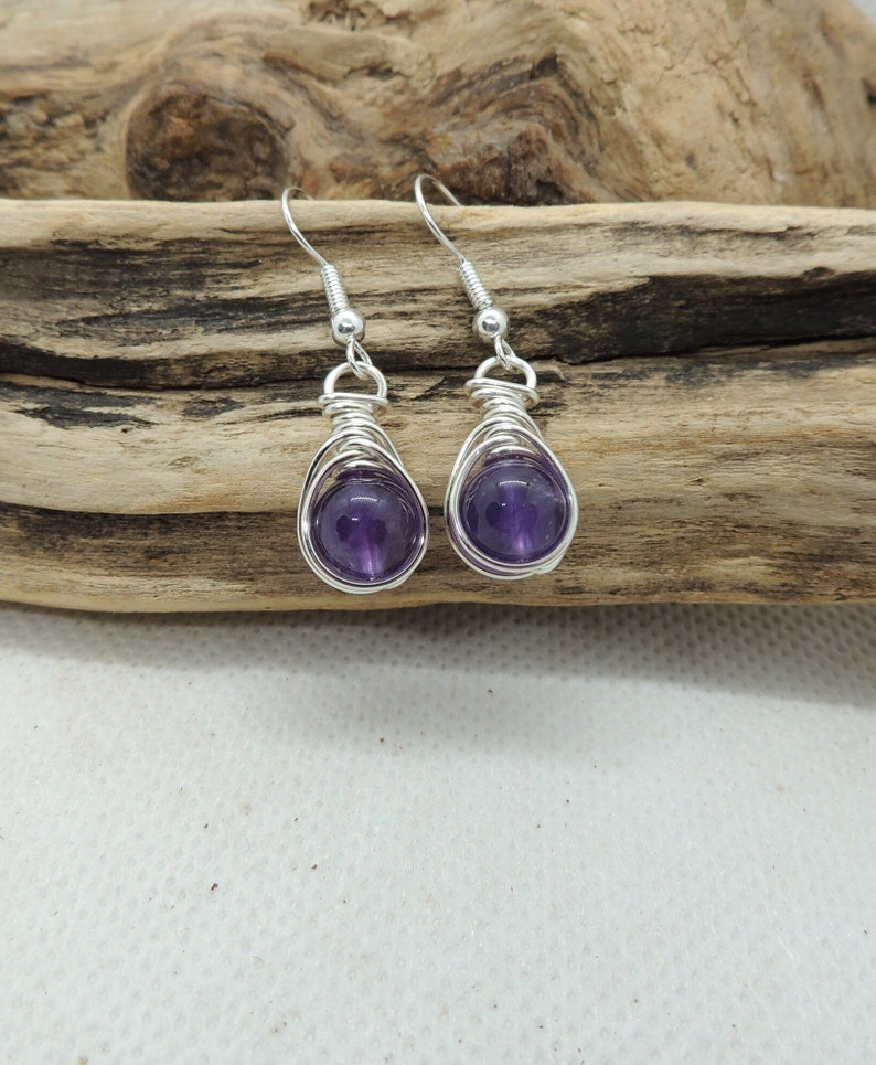 May include: A pair of silver wire wrapped earrings with amethyst gemstones. The earrings are dangle style and have a simple design.