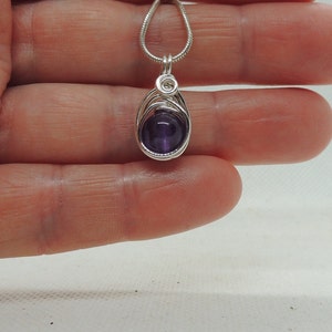 May include: A silver chain necklace with a purple amethyst stone pendant wrapped in silver wire.