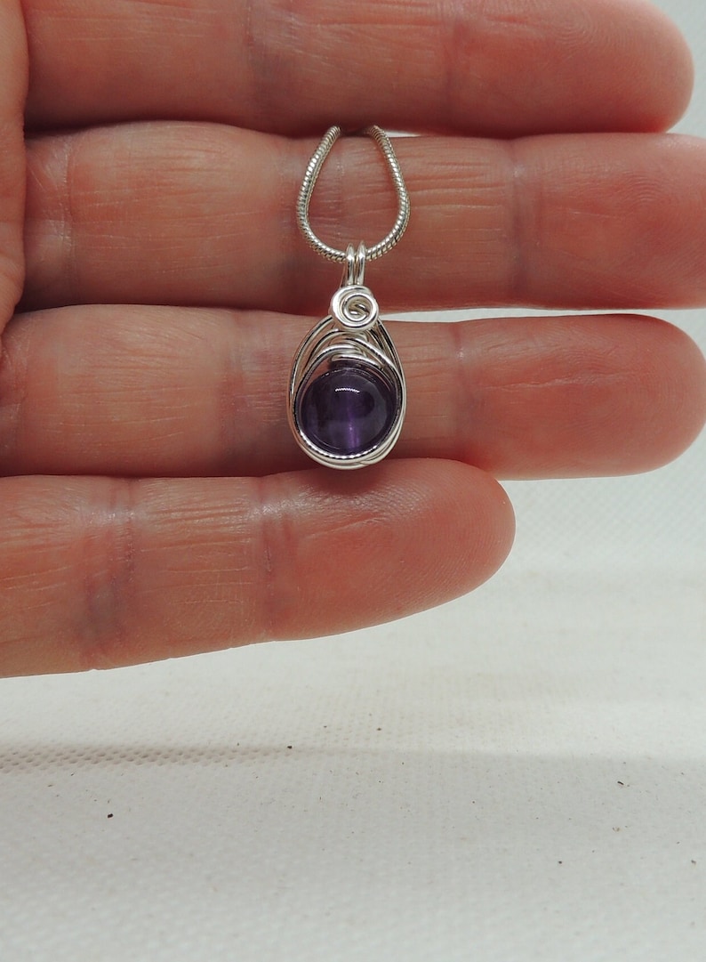 May include: A silver chain necklace with a purple amethyst stone pendant wrapped in silver wire.