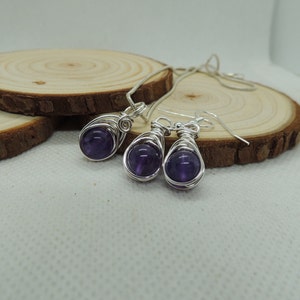 May include: A silver necklace and earrings set with amethyst stones wrapped in silver wire. The stones are a deep purple color.