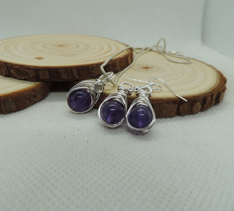 May include: A silver necklace and earrings set with amethyst stones wrapped in silver wire. The stones are a deep purple color.