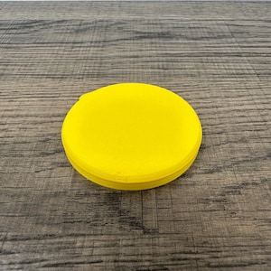 May include: A bright yellow, circular object with a slightly textured surface. The object is a solid color and appears to be made of a single piece of material. The item is sitting on a wooden surface.