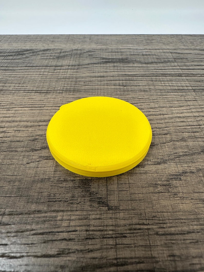 May include: A bright yellow, circular object with a slightly textured surface. The object is a solid color and appears to be made of a single piece of material. The item is sitting on a wooden surface.