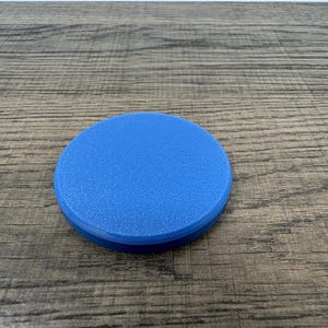 May include: A round, solid blue object with a textured surface. The object is a coaster, made of a durable material, and is designed to protect surfaces from spills and heat. The coaster is approximately 4 inches in diameter.