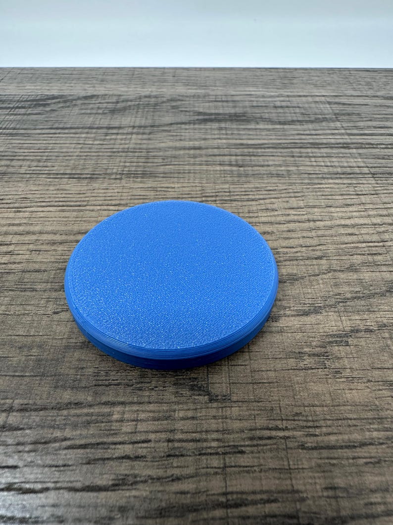May include: A round, solid blue object with a textured surface. The object is a coaster, made of a durable material, and is designed to protect surfaces from spills and heat. The coaster is approximately 4 inches in diameter.