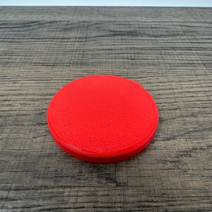 May include: A bright red, circular object with a textured surface. The object is a solid color and appears to be made of a single material. The item is sitting on a wooden surface.