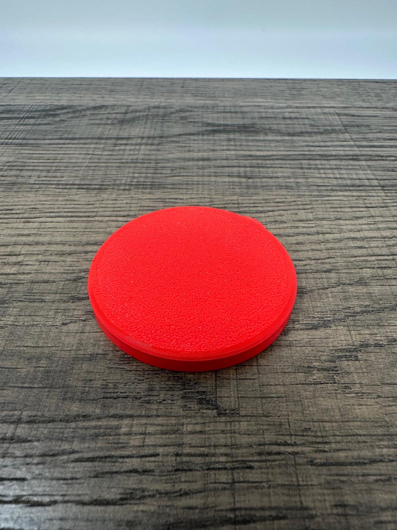 May include: A bright red, circular object with a textured surface. The object is a solid color and appears to be made of a single material. The item is sitting on a wooden surface.