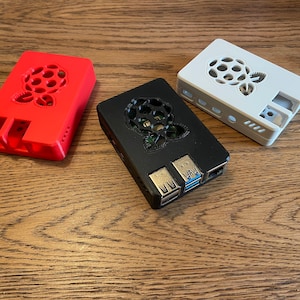 Peut inclure: Trois boîtiers Raspberry Pi en rouge, noir et blanc. Chaque boîtier présente une découpe en forme de logo Raspberry Pi sur le dessus.