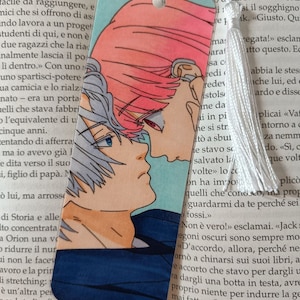 Può includere: Segnalibro con un'illustrazione in stile anime di due figure vicine, con capelli rosa e bianchi e dettagli blu. Ha un nappa bianca e una base blu.