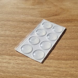 May include: A sheet of clear adhesive pads, arranged in a grid pattern on a white backing. There are 12 pads in total.