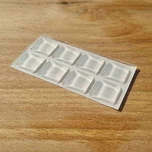 May include: A sheet of clear adhesive squares, designed to protect surfaces from scratches and damage. The squares are arranged in a grid pattern.