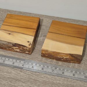 Pode incluir: Duas bases de madeira artesanais com bordas naturais. As bases são retangulares, com um esquema de cores castanho claro e creme. Uma régua de metal está colocada perto das bases.