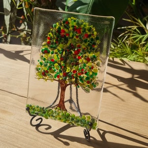 Könnte beinhalten: Ein Glaskunstwerk, das einen Baum mit grünen Blättern und roten Früchten darstellt. Der Baum steht auf einem Ständer mit grünem Sockel.