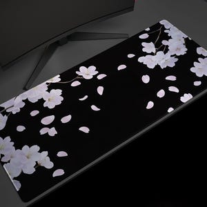 May include: Black mouse pad with a white cherry blossom design. The blossoms are scattered across the pad and some petals are falling.