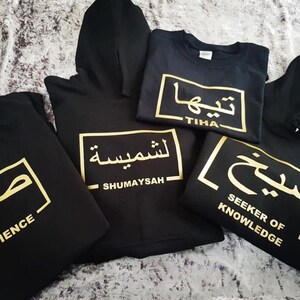 Puede incluir: Cuatro sudaderas con capucha negras y una camiseta con caligraf&iacute;a &aacute;rabe dorada y traducciones al ingl&eacute;s. Las palabras son "Paciencia", "Shumaysah", "Tiha" y "Buscador de Conocimiento".