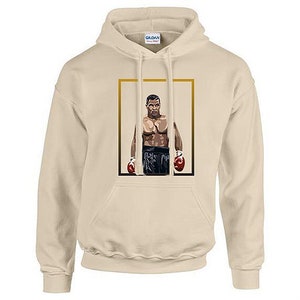 May include: A beige hoodie with a gold frame featuring a drawing of a boxer wearing red boxing gloves. The text "Gildan" is visible on the hoodie.