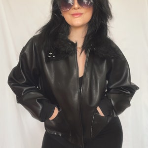 Puede incluir: Una chaqueta bomber negra de imitación de cuero con cuello de piel y cierre de cremallera. La chaqueta tiene dos bolsillos en la parte delantera y puños de canalé.