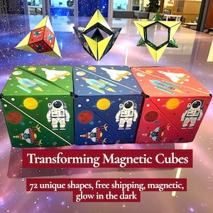 Pode incluir: Cubos magnéticos transformáveis em verde, azul e vermelho com ilustrações temáticas espaciais. Os cubos transformam-se em várias formas geométricas. A imagem também mostra os cubos em diferentes formas transformadas.