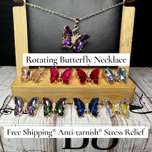 Op de afbeelding: Een goudkleurige ketting met een draaiende vlinderhanger, samen met verschillende vlindervormige oorbellen in verschillende kleuren. De tekst "Rotating Butterfly Necklace" is zichtbaar. De oorbellen zijn in tinten roze, rood, blauw en helder.