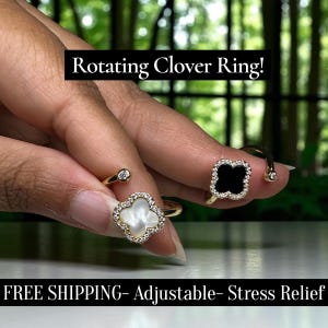 May include: Gold-coloured rotating clover rings, one with a white clover and the other with a black clover design, both with small, sparkling stones. The rings are displayed on a hand, with the text "Rotating Clover Ring!" in a black banner.
