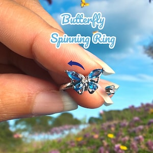 May include: A silver ring with a blue butterfly design. The butterfly's wings are set with blue gemstones and the ring is designed to spin.