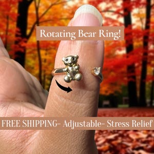 May include: A gold-colored rotating bear ring. The ring features a small bear charm that spins. The ring is adjustable and has a small heart-shaped accent on the opposite side. The text "Rotating Bear Ring!" is displayed above the ring.
