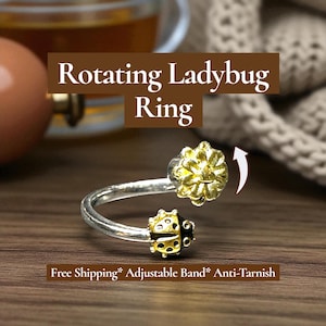 May include: A silver-toned ring with a rotating ladybug design. The ring features a gold-colored flower and a ladybug with black and yellow accents. The text "Rotating Ladybug Ring" is displayed above the ring.