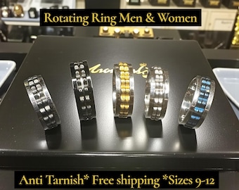 May include: Five rotating rings with a silver finish, black finish, and gold finish are displayed. One ring has a blue inlay. The text "Rotating Ring Men & Women" is at the top. The text "Anti Tarnish" is at the bottom.