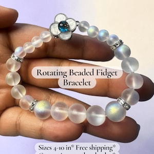 May include: A beaded bracelet with a rotating flower-shaped charm. The bracelet features iridescent, frosted beads and silver-toned accents. The text on the image reads "Rotating Beaded Fidget Bracelet".