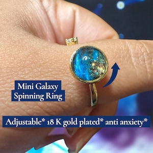 May include: A gold-plated, adjustable ring with a spinning galaxy design. The ring features a round, blue and gold galaxy-themed center. Text on the image reads "Mini Galaxy Spinning Ring" and "Adjustable* 18 K gold plated* anti anxiety*."
