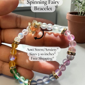 May include: A colorful beaded bracelet with the text "Spinning Fairy Bracelet." The bracelet features a flower charm and gold-colored accents. The beads transition through shades of yellow, green, blue, and pink. The bracelet is approximately 5-10 inches in length.