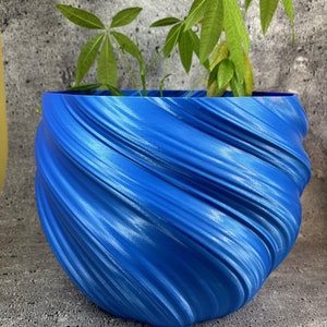 Puede incluir: Una maceta de cerámica azul en forma de espiral con una planta verde en su interior. La maceta tiene un acabado liso y brillante.