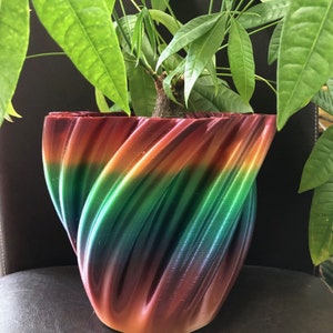 Puede incluir: Una maceta de cerámica colorida, con forma de espiral, de colores arcoíris, con una planta verde en su interior.